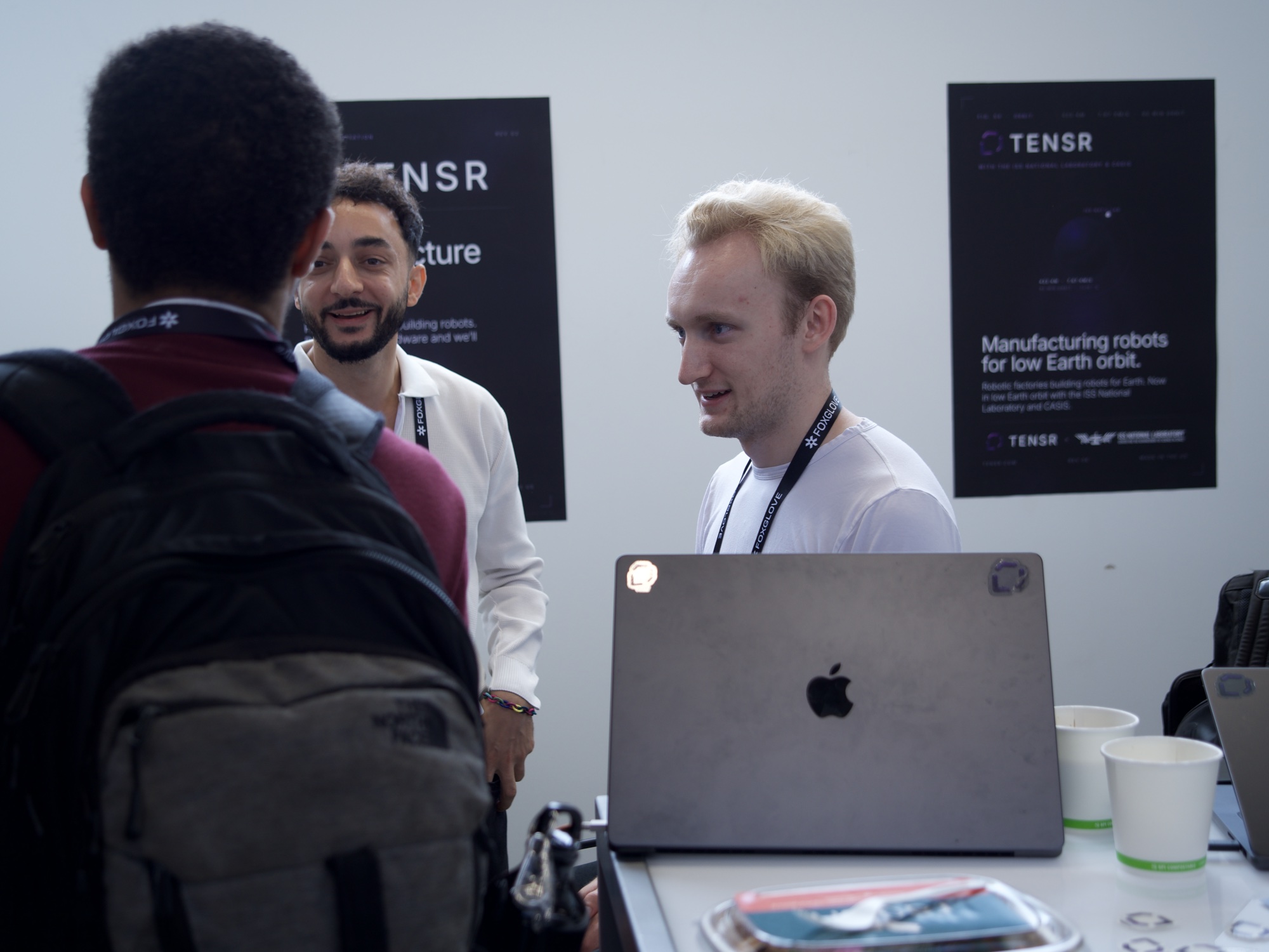 Two founders talking with a visitor over a sticker-covered laptop at the booth