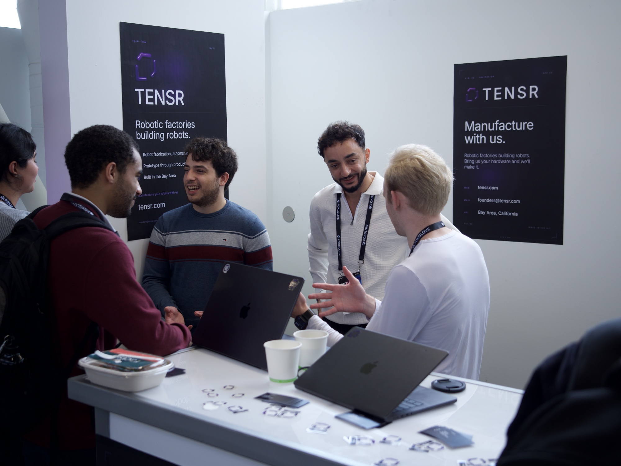 The Tensr founders and visitors around the booth table, TENSR posters on both walls