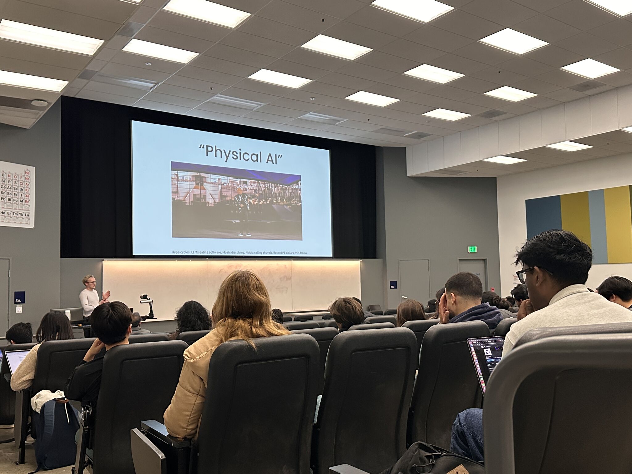 The lecture hall from the back rows, a "Physical AI" slide on the screen